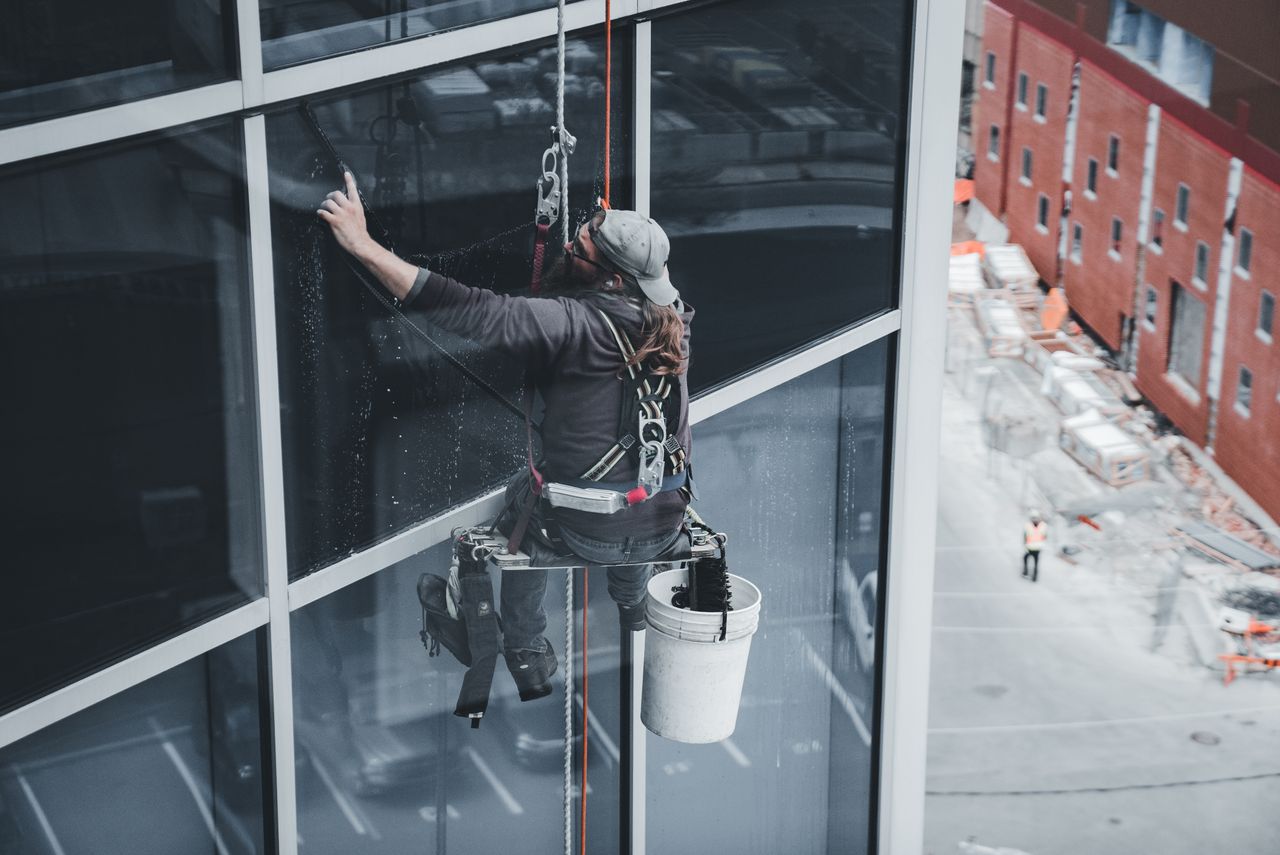 A worker cleaning skyscraper windows with a harness in an urban setting.